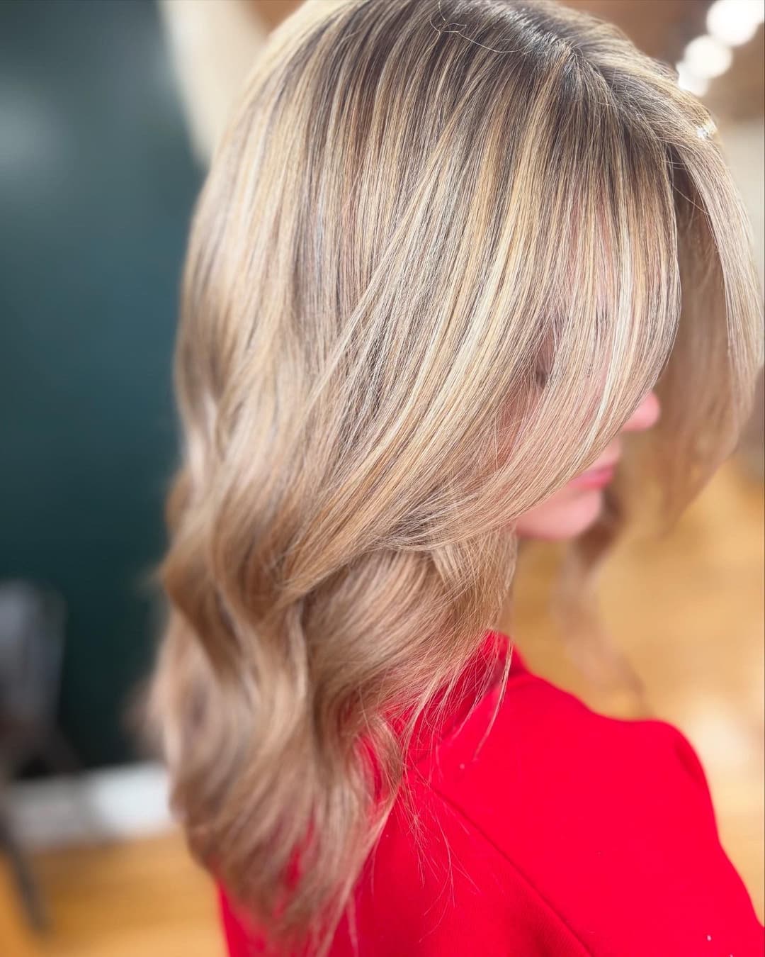 Stylish woman with wavy blonde hair in a red top, showcasing vibrant hair color and texture.