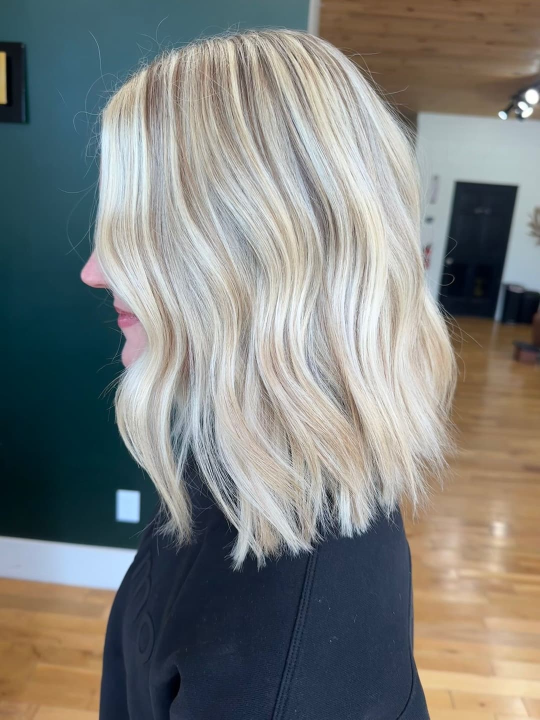Woman with blonde wavy hair showing textured shoulder-length hairstyle in salon setting.