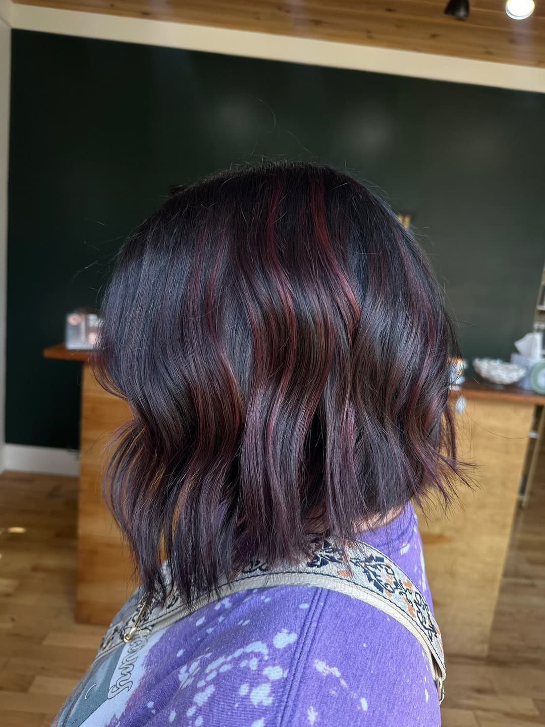 Stylish wavy bob haircut with hints of red highlights on a dark background.