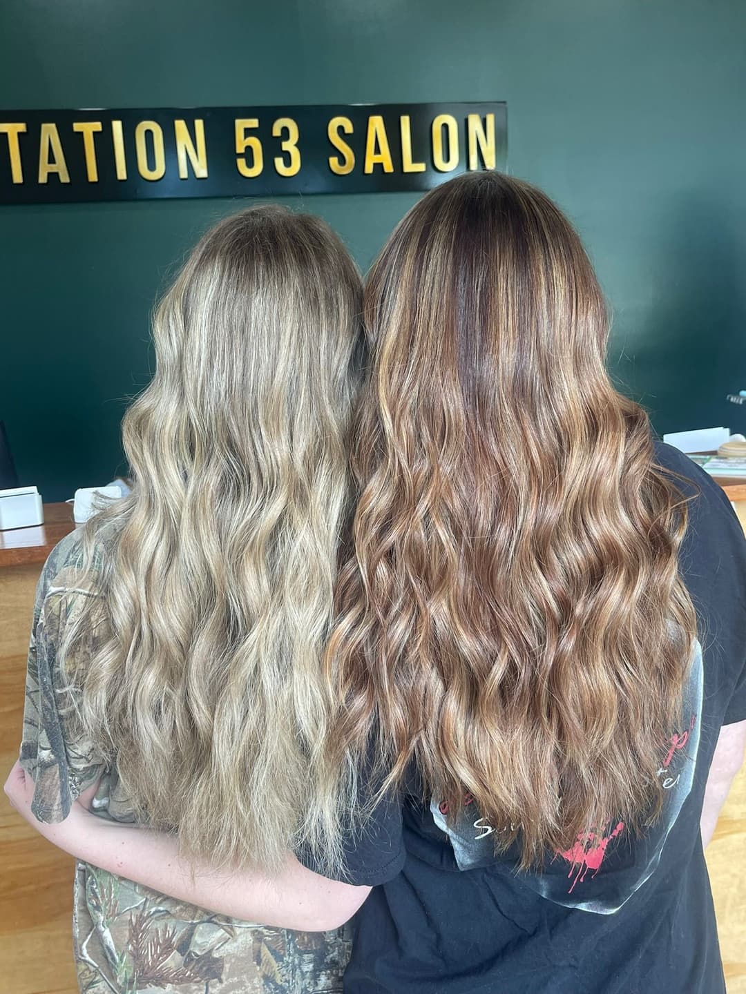 Two women with wavy hair standing side by side in a salon, showcasing different hair colors.