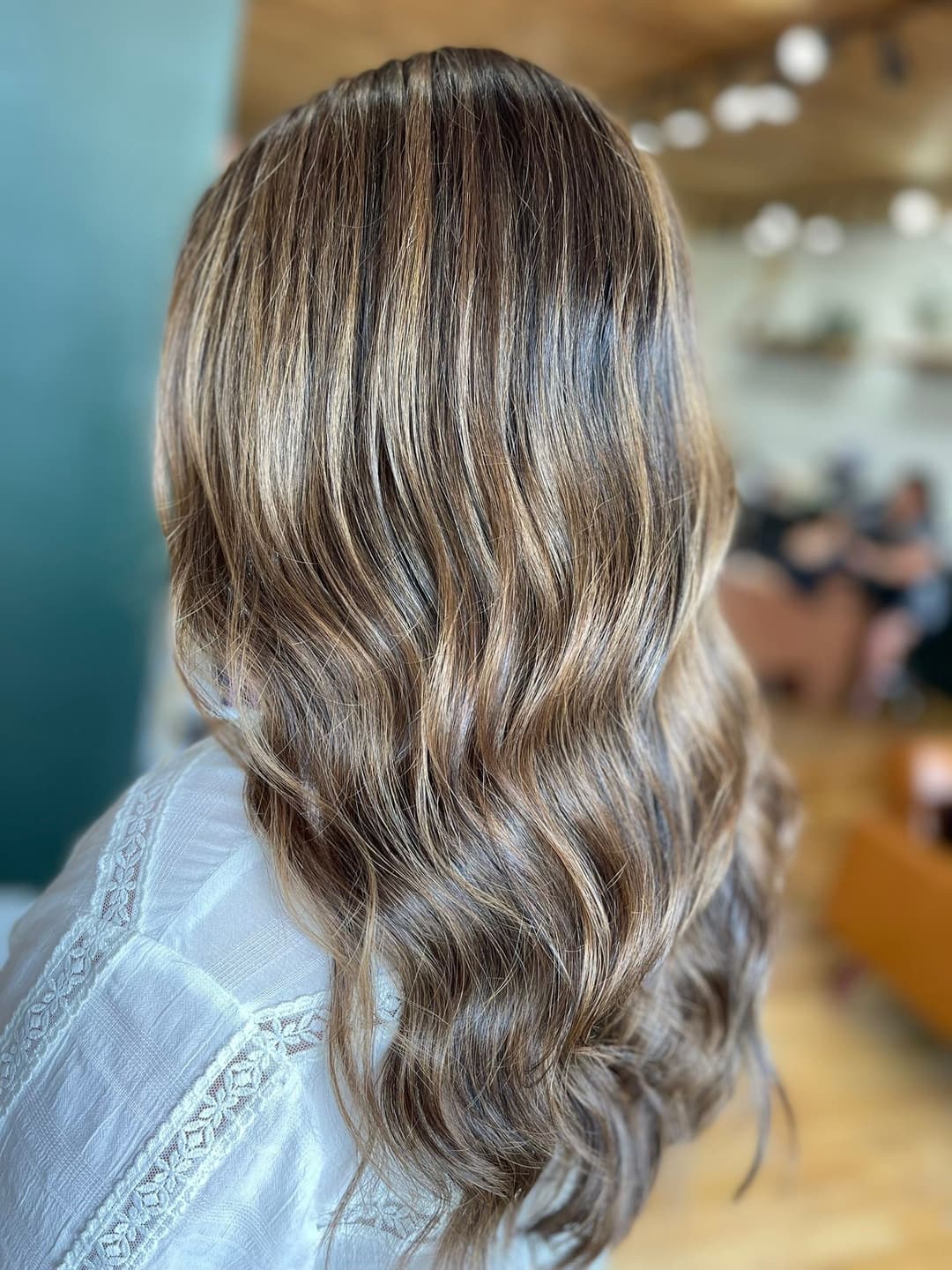 Wavy, shoulder-length hair with caramel highlights in a modern salon setting.