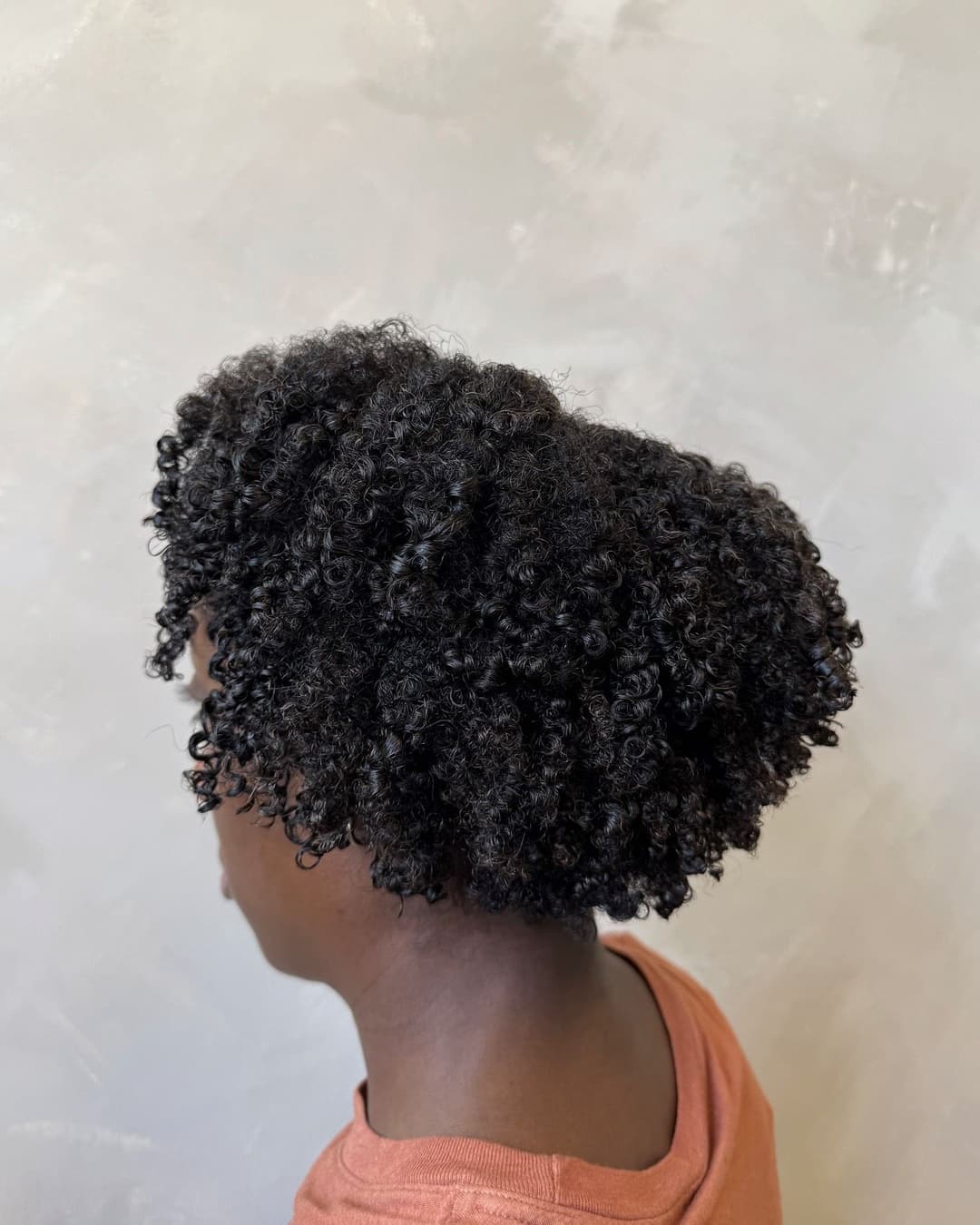 Curly black hairstyle on a child showcasing defined, bouncy curls against a textured background.