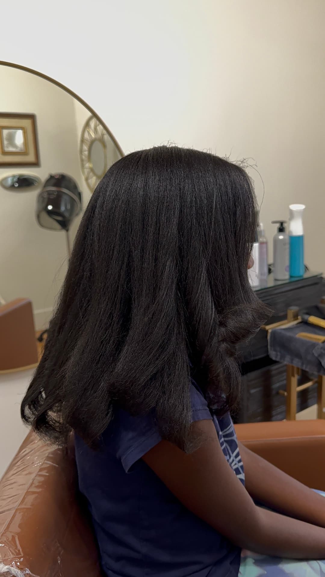 Child with sleek, straightened black hair sitting in a salon chair, side profile view.