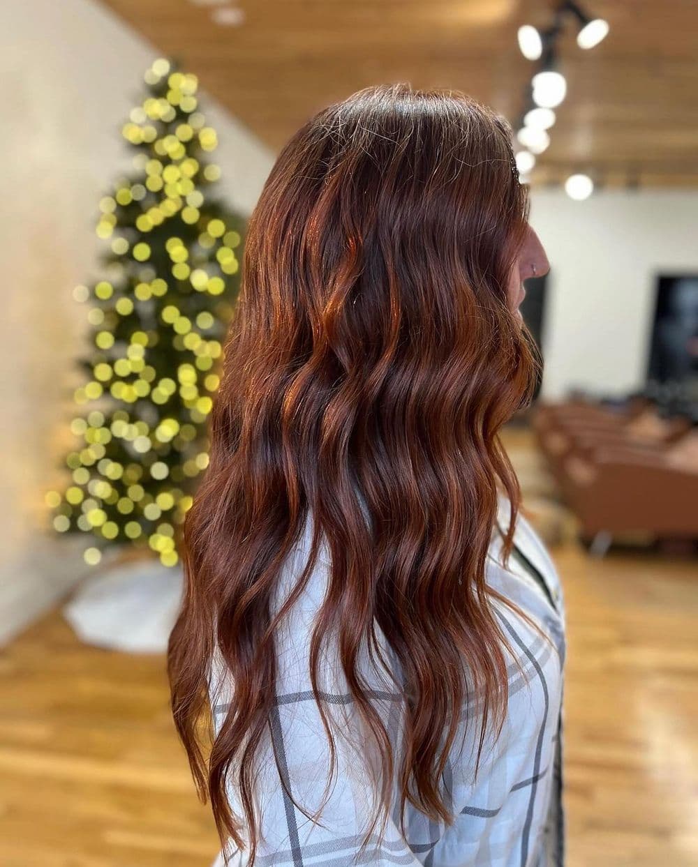 Woman with wavy, chestnut-colored hair beside a decorated Christmas tree.