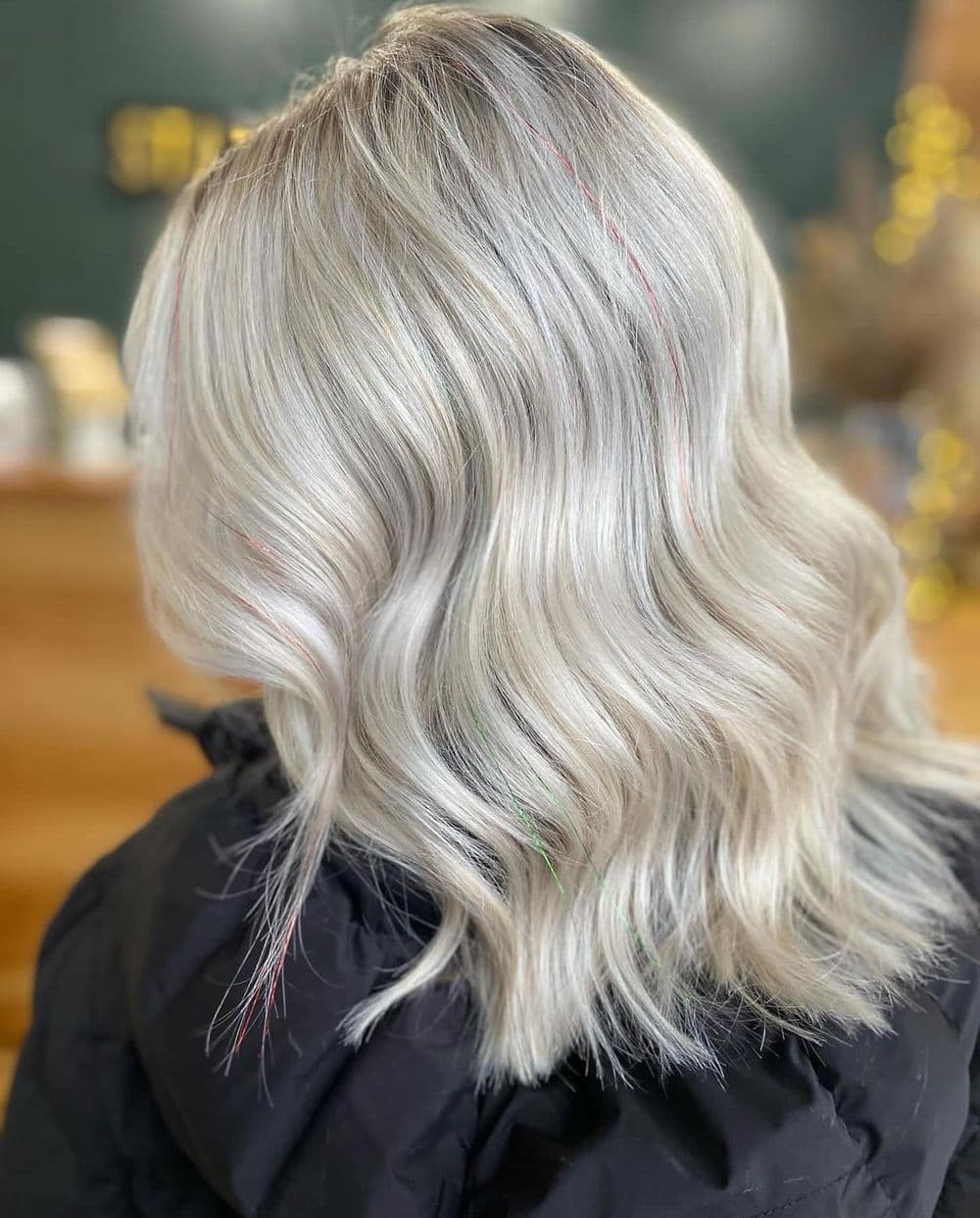 Wavy platinum blonde hair with colorful highlights in a cozy salon setting.