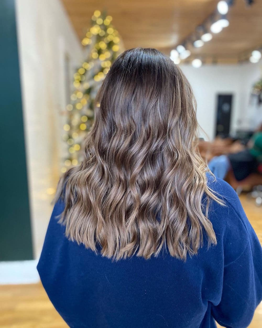 Woman with wavy, shoulder-length hair showing balayage highlights in a salon setting.