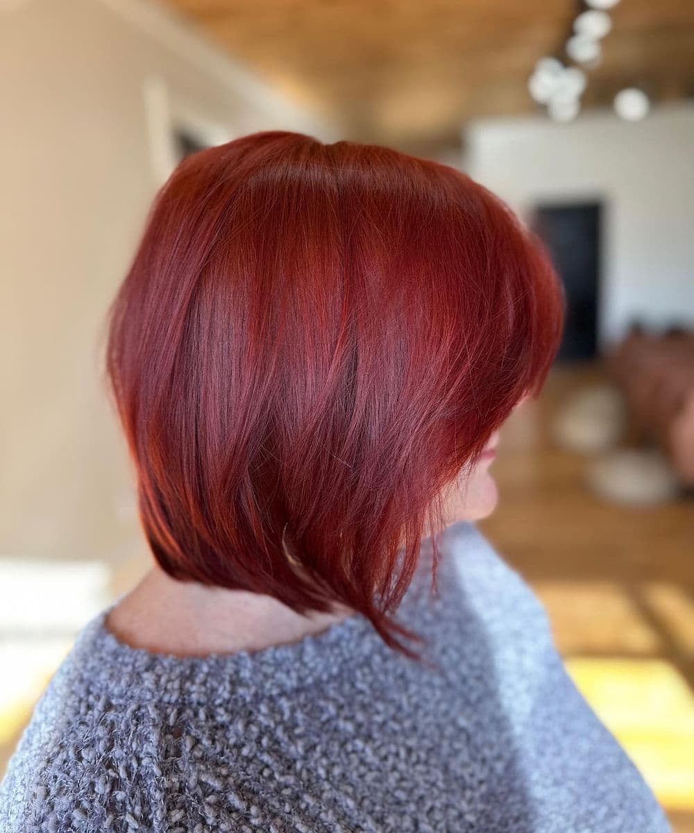 Woman with vibrant red bob haircut in a cozy indoor setting.